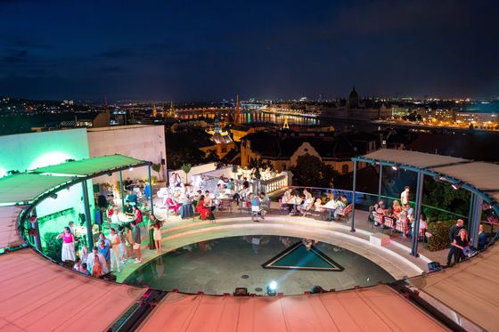 Evening event on the Aranybástya terrace with coloured lights above the lit city