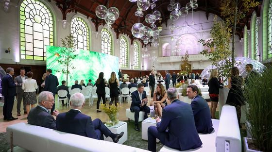 Guests in the riding hall with a green stage backdrop and hanging lights