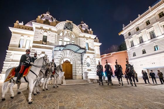 Hussars on horseback in front of the lit Royal Riding Hall at night